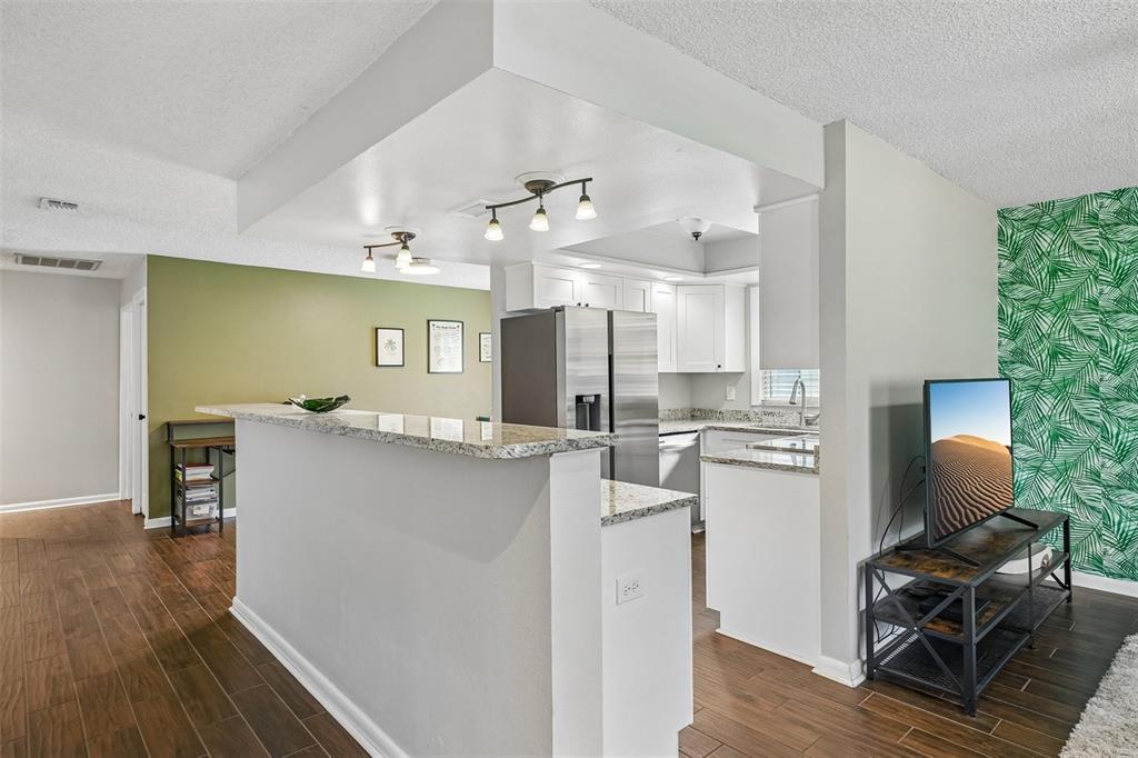 A kitchen with white cabinets and granite countertops overlooks a living area with palm wallpaper — 4717 W PRESCOTT STREET, TAMPA, FL