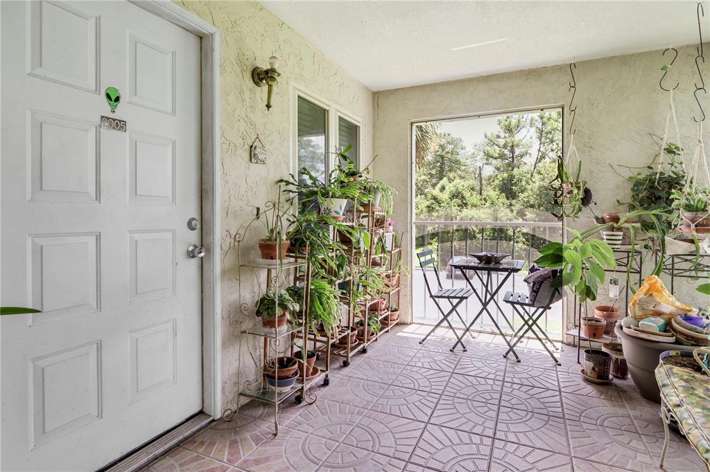 A covered patio features tiled flooring, a metal plant stand, and a small bistro set — 2005 NORTHLAKE DRIVE, SANFORD, FL