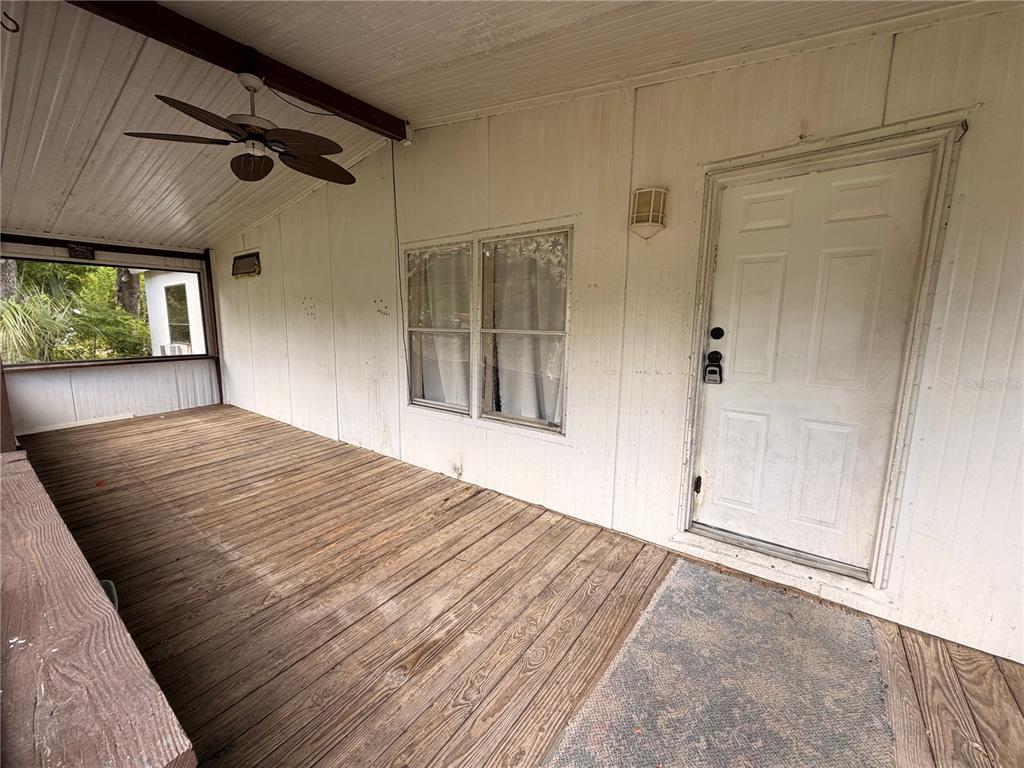 A covered wooden porch features a ceiling fan, white paneled walls, and a white door — 24021 ARMADILLO ROAD, ASTOR, FL