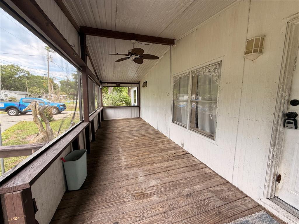 A covered wooden porch features a ceiling fan, screened walls, and a white exterior door — 24021 ARMADILLO ROAD, ASTOR, FL
