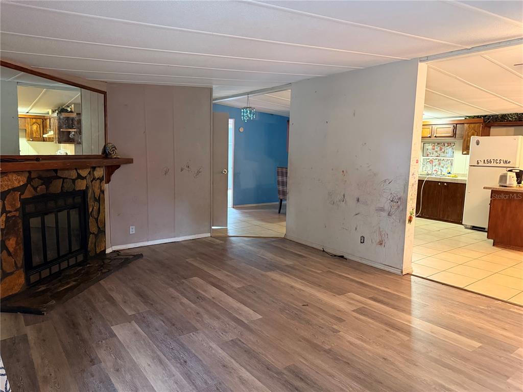 A living room with wood-look flooring, a stone fireplace, and an adjacent kitchen area — 24021 ARMADILLO ROAD, ASTOR, FL
