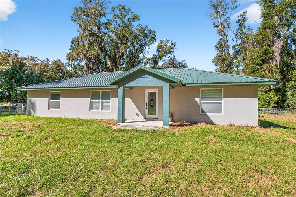 A single-story house with a green metal roof sits behind a chain-link fence — 201 N WEST STREET, INTERLACHEN, FL