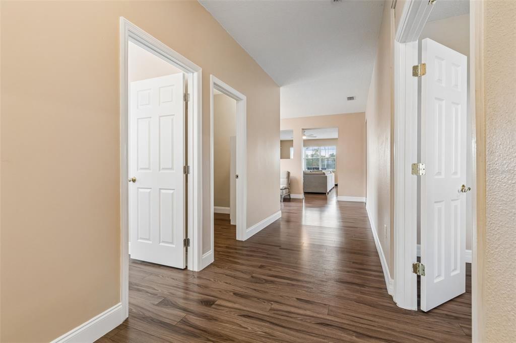 A hallway with wood-look flooring leads to an open living area with multiple white doors — 5405 HAMMOCK VIEW LANE, APOLLO BEACH, FL
