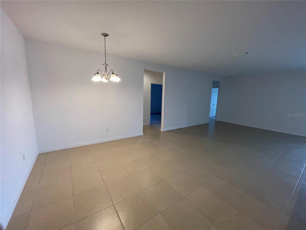 An empty dining area with tile flooring and a hanging light fixture leads to hallways — 5566 SABAL DRIVE, ST CLOUD, FL