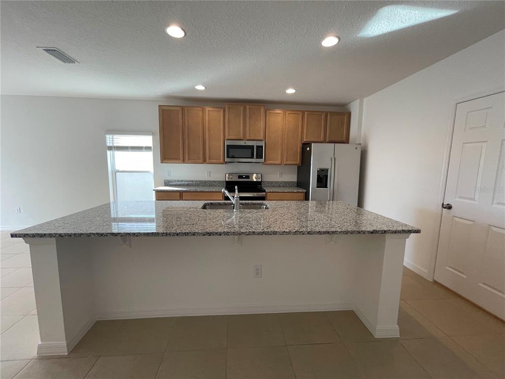 A kitchen features light wood cabinets, granite countertops, a large island, and stainless steel appliances — 5566 SABAL DRIVE, ST CLOUD, FL