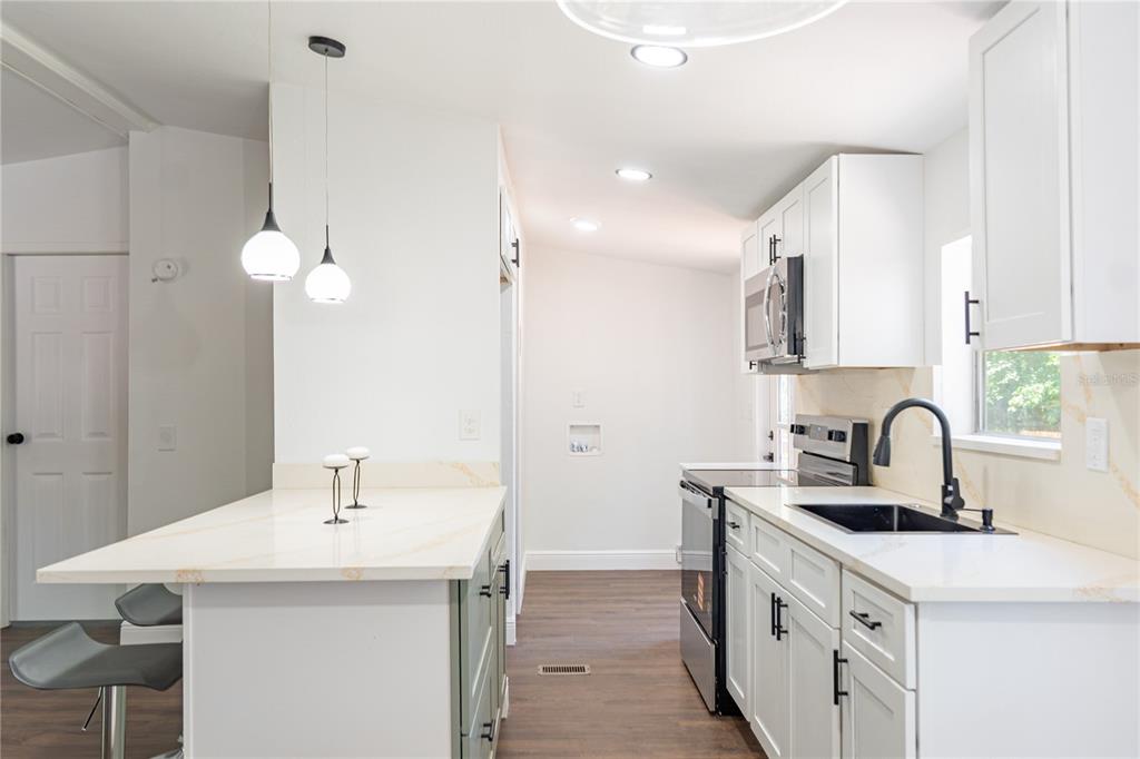A kitchen with white cabinets, quartz countertops, a black sink, and an adjacent laundry area — 1809 NE 162ND STREET, CITRA, FL