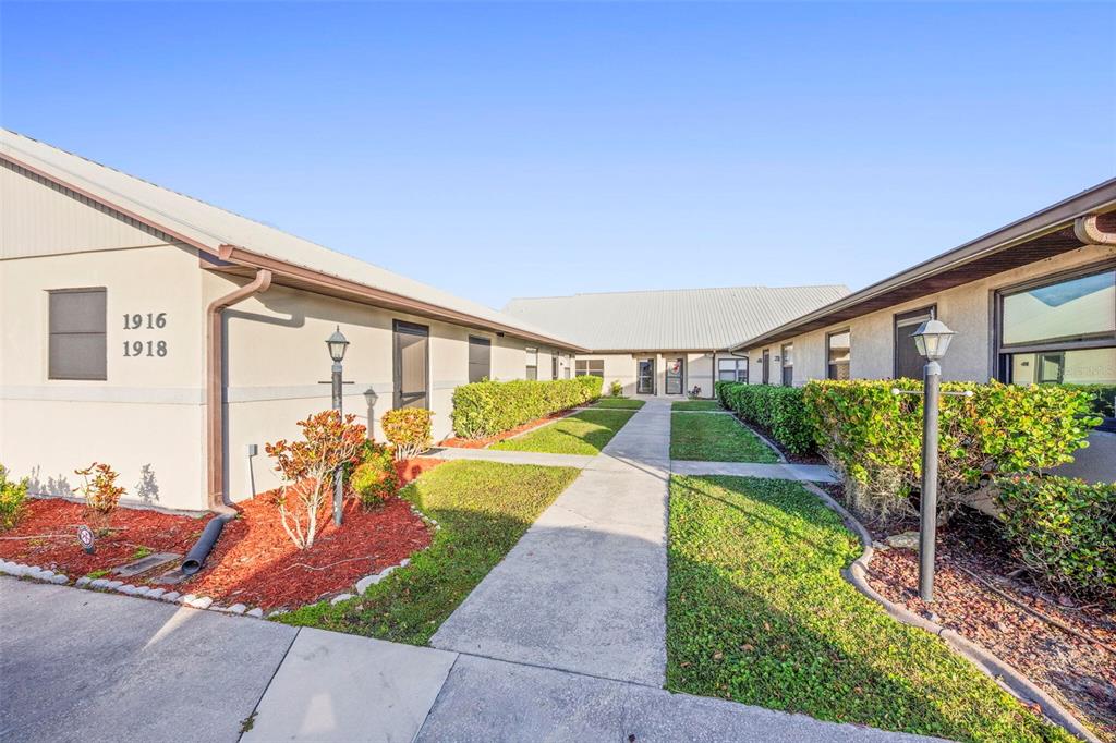 A concrete walkway leads between two single-story apartment buildings with landscaped hedges and red mulch — 1916 VILLAWAY E, SEBRING, FL