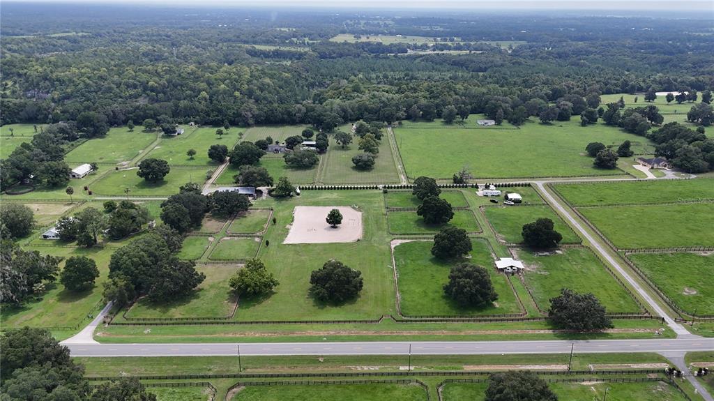 An aerial view of a rural property featuring fenced pastures, several buildings, and mature trees — 13489 NW GAINESVILLE ROAD, REDDICK, FL