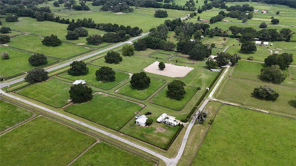 An aerial view of a rural property featuring fenced pastures, several trees, and a small house — 13489 NW GAINESVILLE ROAD, REDDICK, FL