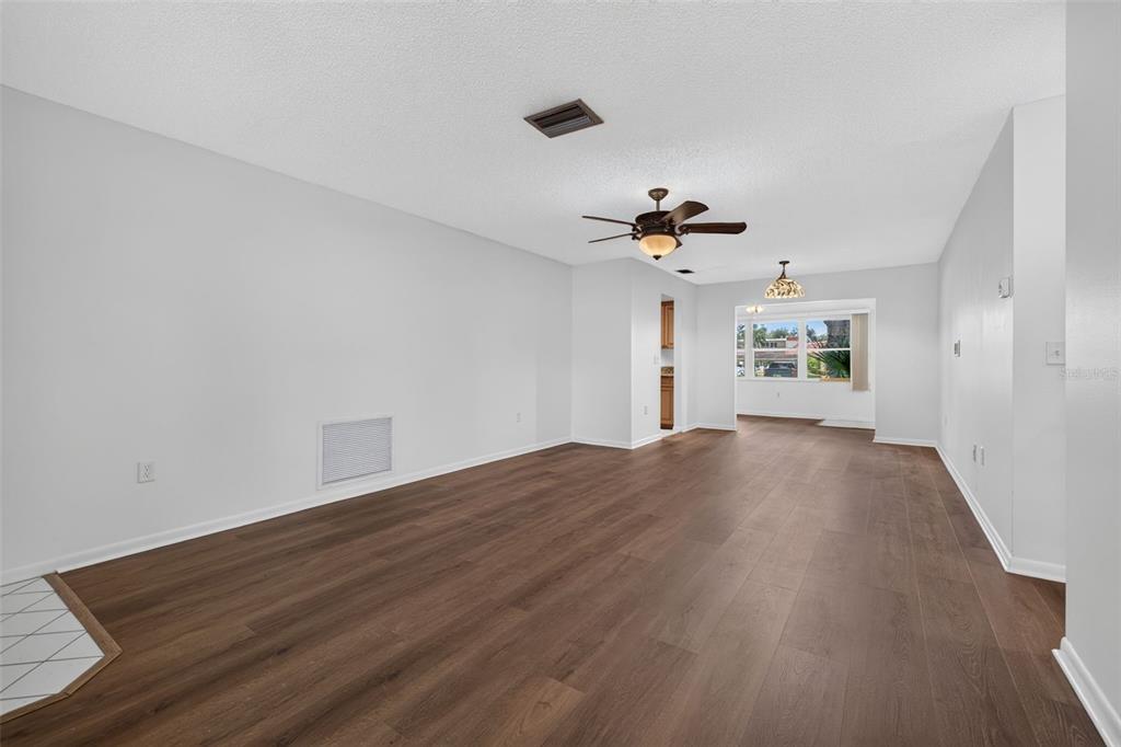 An empty room with wood-look flooring, a ceiling fan, and a view into a kitchen — 12200 VONN ROAD UNIT 7D, LARGO, FL