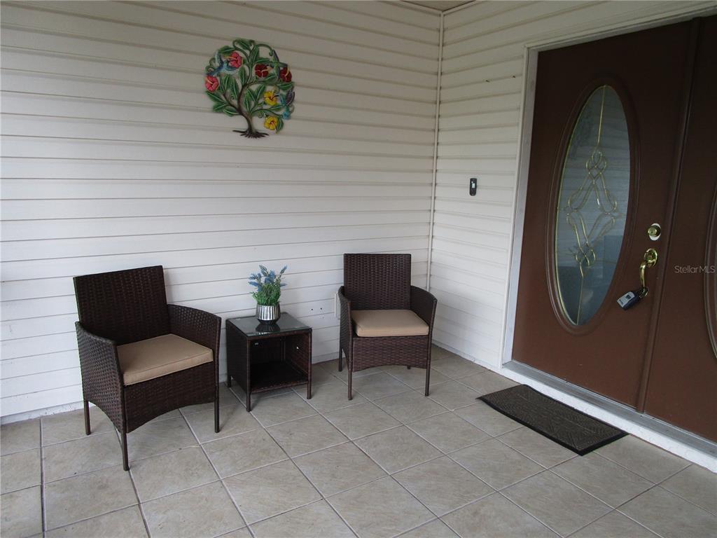 A covered porch features tiled flooring, two wicker chairs, a small table, and a front door — 7401 GALLOWAY ROAD, WEEKI WACHEE, FL