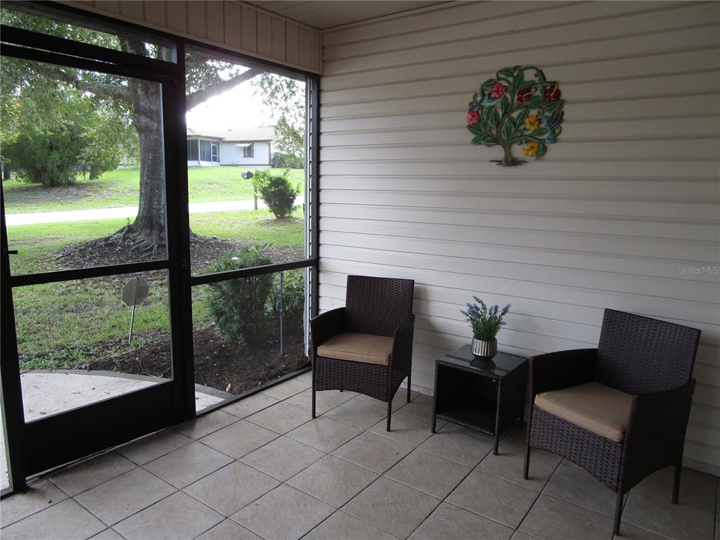 A screened-in porch features tiled flooring, two wicker chairs, a small table, and wall decor — 7401 GALLOWAY ROAD, WEEKI WACHEE, FL