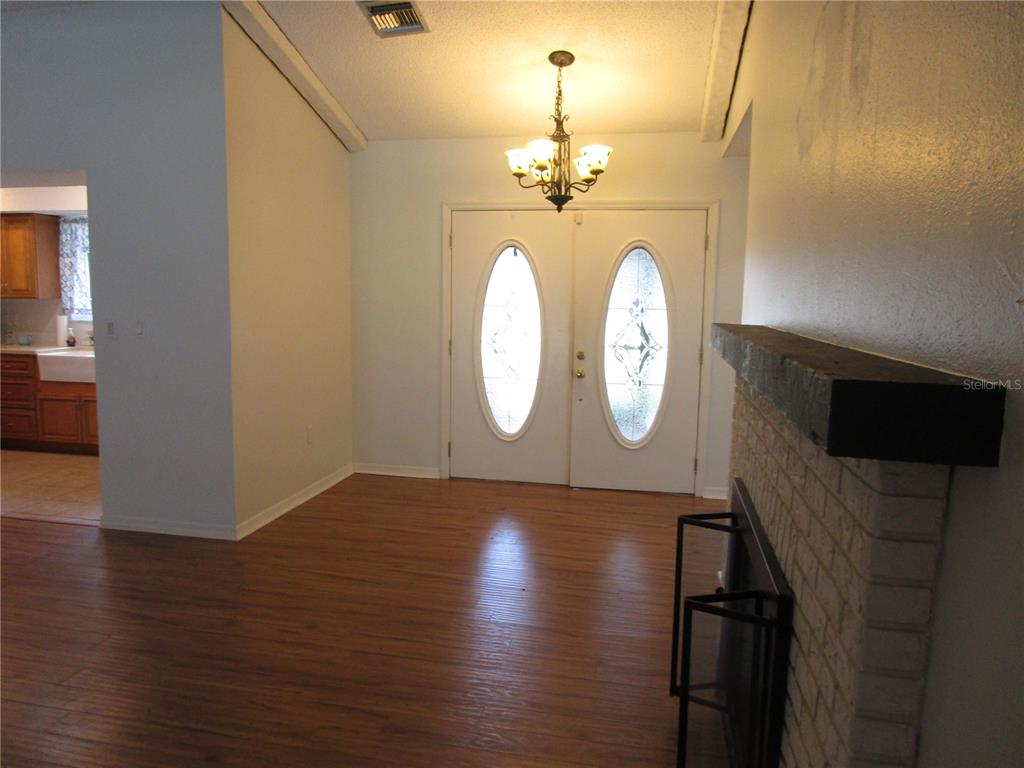 A room with wood-look flooring, a brick fireplace, and double front doors with glass inserts — 7401 GALLOWAY ROAD, WEEKI WACHEE, FL
