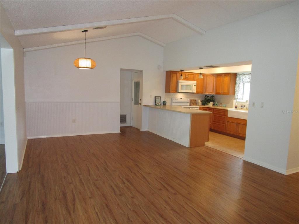 A living area with wood-look flooring opens to a kitchen featuring wood cabinets and counters — 7401 GALLOWAY ROAD, WEEKI WACHEE, FL