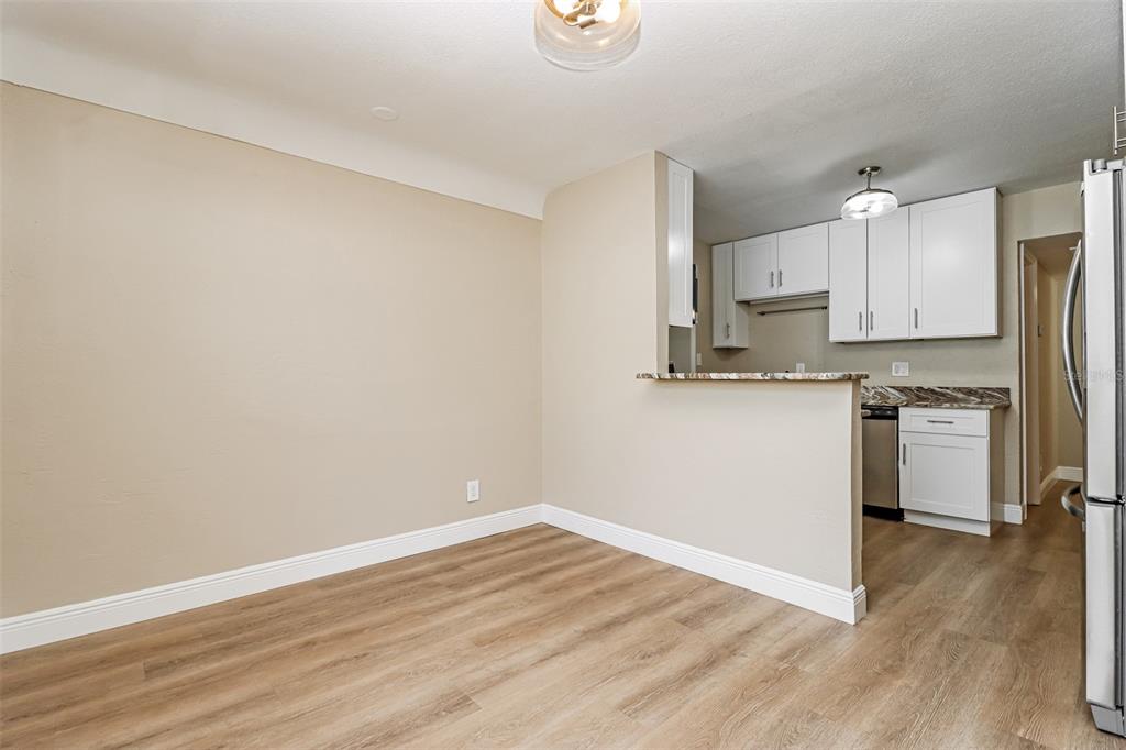An empty dining area with wood-look flooring opens into a kitchen with white cabinets — 10293 SATSUMA ROAD, SEMINOLE, FL