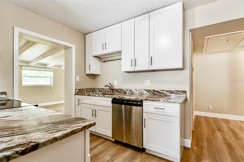 A kitchen features white cabinets, granite countertops, and stainless steel appliances over wood-look flooring — 10293 SATSUMA ROAD, SEMINOLE, FL