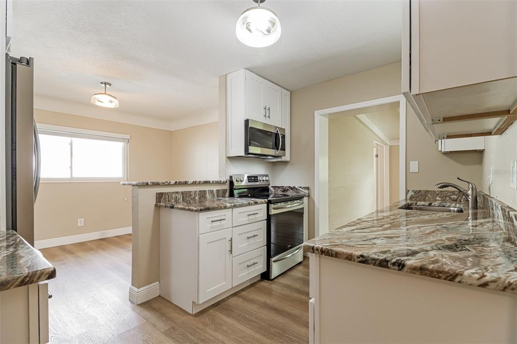 A kitchen with white cabinets, granite countertops, stainless steel appliances, and wood-look flooring — 10293 SATSUMA ROAD, SEMINOLE, FL