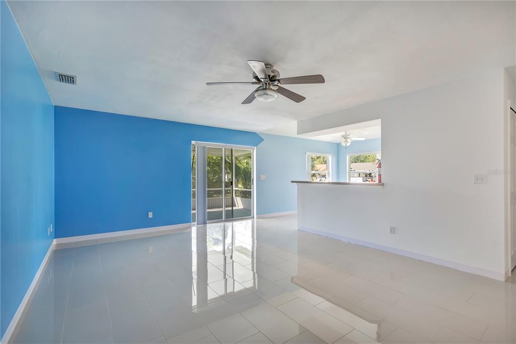 A bright living room features light blue walls, white tile flooring, and a sliding glass door — 561 15TH STREET, HOLLY HILL, FL