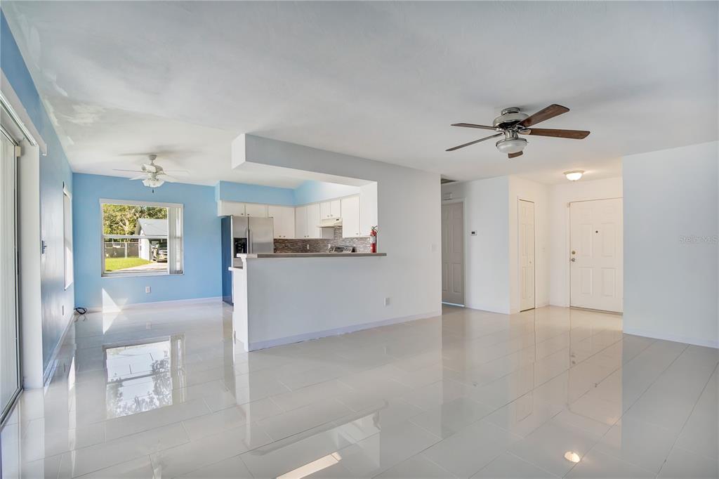 A bright living room with white tile floors, a ceiling fan, and an open kitchen — 561 15TH STREET, HOLLY HILL, FL