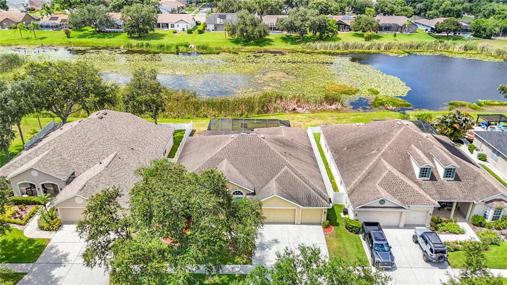 An aerial view shows three suburban houses with brown roofs situated along a pond — 8511 NORTHTON GROVES BOULEVARD, ODESSA, FL