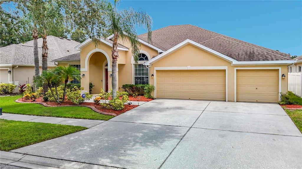 A single-story house with a tan stucco exterior, a three-car garage, and a landscaped front yard — 8511 NORTHTON GROVES BOULEVARD, ODESSA, FL