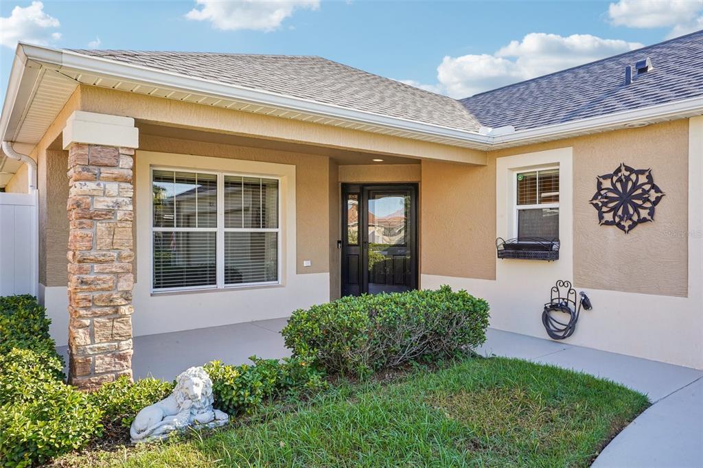 The exterior of a tan house features a stone-clad pillar, a front porch, and landscaping — 583 ARTEAGA WAY, THE VILLAGES, FL