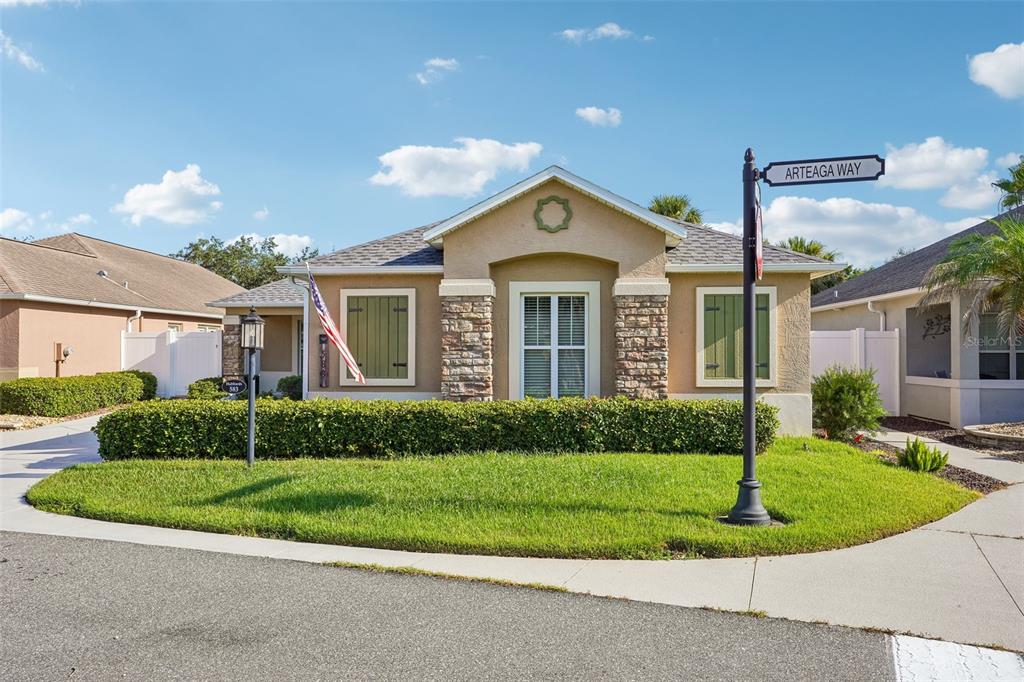 A single-story house with a tan stucco exterior, stone accents, and green shutters — 583 ARTEAGA WAY, THE VILLAGES, FL
