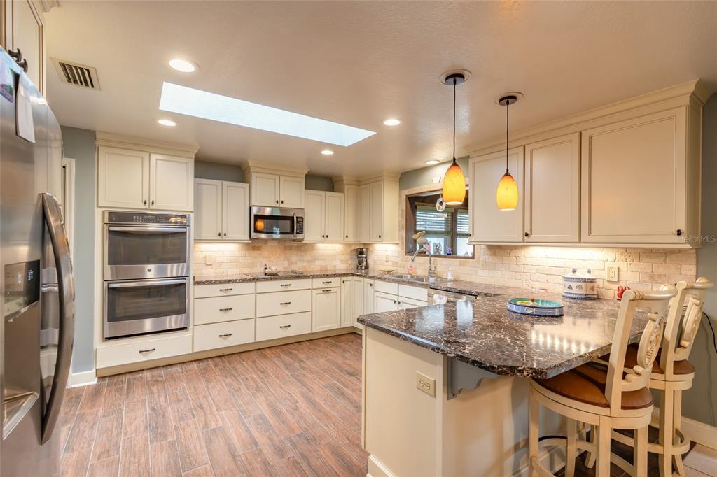 A kitchen with cream cabinets, dark granite countertops, stainless steel appliances, and wood-look tile flooring — 1413 ORANGE TREE DRIVE, EDGEWATER, FL