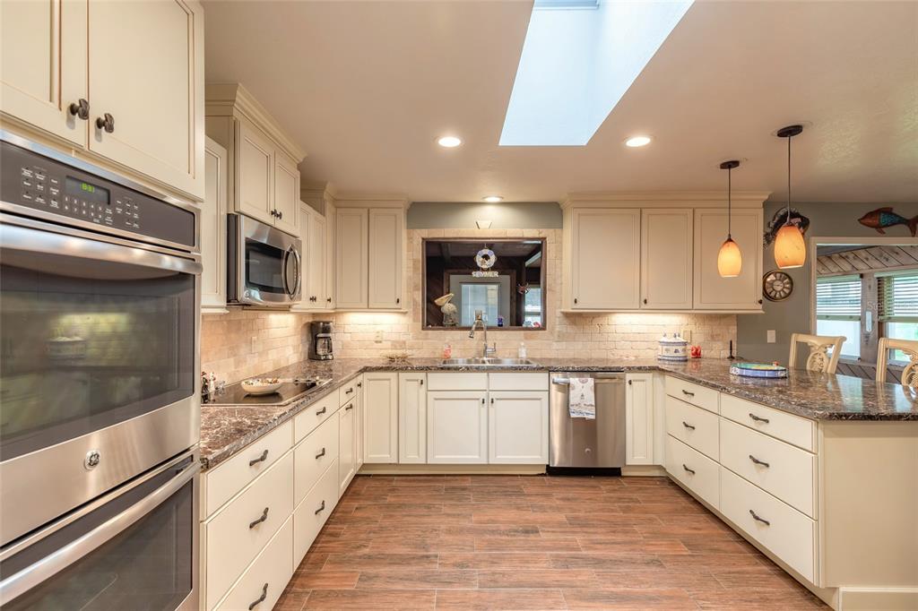 A kitchen features white cabinetry, stainless steel appliances, granite countertops, and a skylight — 1413 ORANGE TREE DRIVE, EDGEWATER, FL