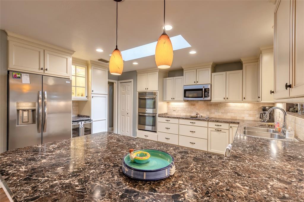 A kitchen with cream cabinets, dark granite countertops, stainless steel appliances, and two pendant lights — 1413 ORANGE TREE DRIVE, EDGEWATER, FL
