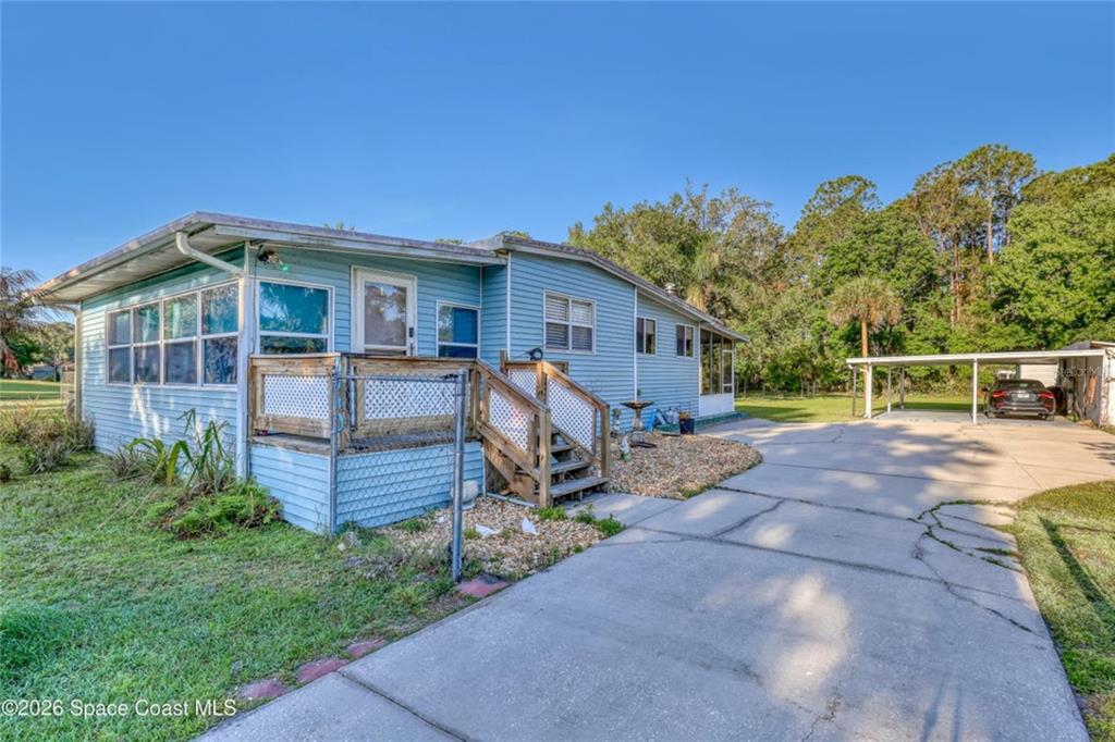 A light blue mobile home with a wooden deck and a detached carport — 2540 TUSCANY DRIVE, MIMS, FL