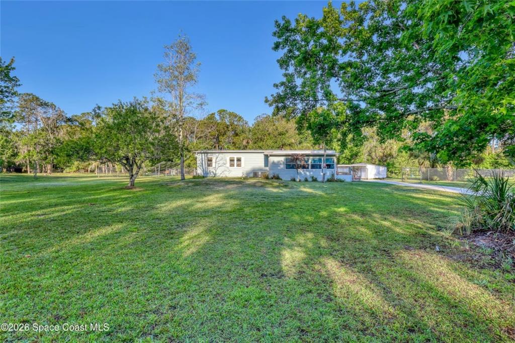 A single-story house with light-colored siding sits on a large, grassy lot with trees — 2540 TUSCANY DRIVE, MIMS, FL