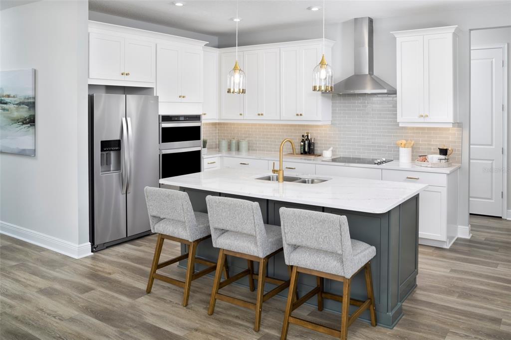 A modern kitchen features white cabinetry, a dark gray island with barstools, and stainless appliances — 34733 FLOWER PATCH DRIVE, DADE CITY, FL
