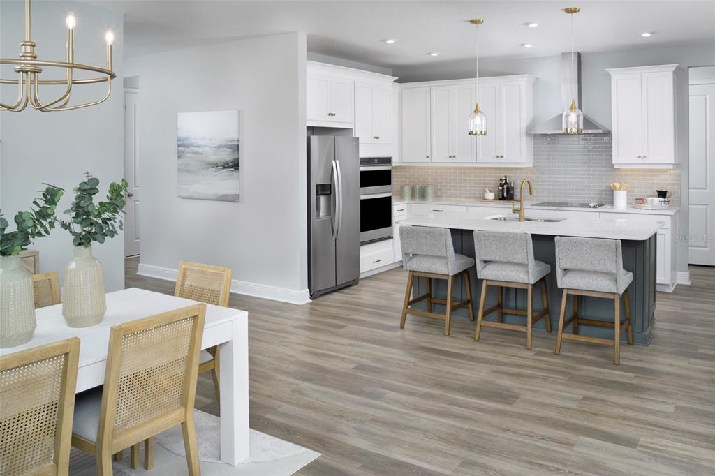A modern kitchen features white cabinetry, a dark gray island with bar seating, and wood-look flooring — 34733 FLOWER PATCH DRIVE, DADE CITY, FL
