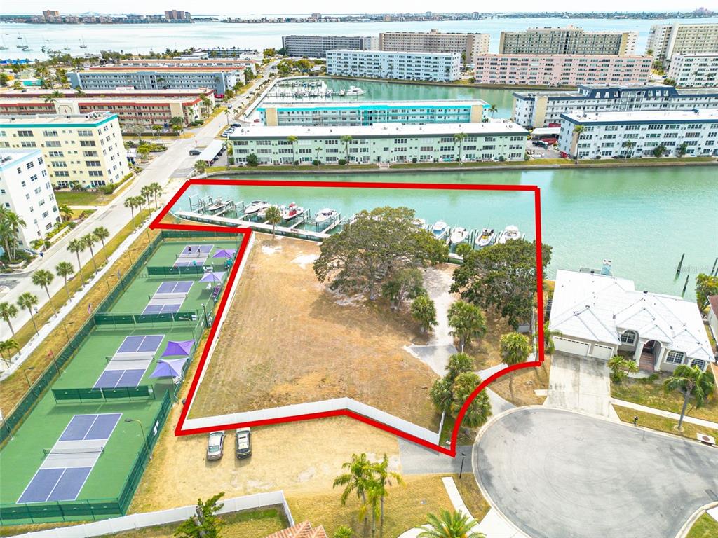 An aerial view shows a vacant waterfront lot with boat slips and adjacent tennis courts — 5814 SKIMMER POINT BOULEVARD S, GULFPORT, FL