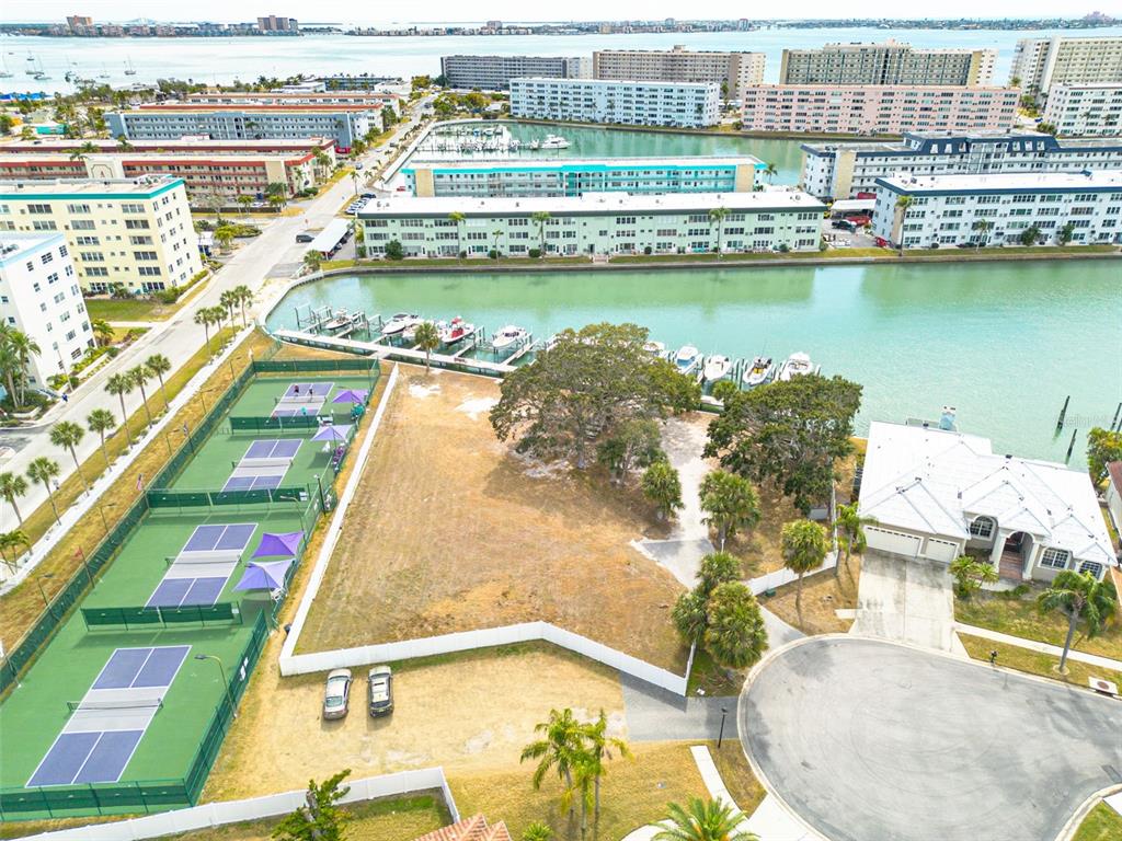 An aerial view shows a vacant lot adjacent to tennis courts, a house, and a canal — 5814 SKIMMER POINT BOULEVARD S, GULFPORT, FL
