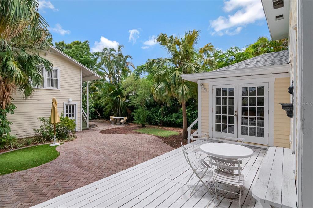 A backyard features a brick patio, a white wooden deck, and two yellow siding buildings — 126 8TH AVENUE NE UNIT 1/2, ST PETERSBURG, FL