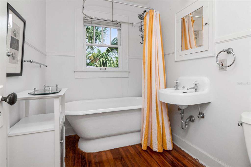 A bathroom features a clawfoot tub, a wall-mounted sink, and a yellow-striped shower curtain — 126 8TH AVENUE NE UNIT 1/2, ST PETERSBURG, FL