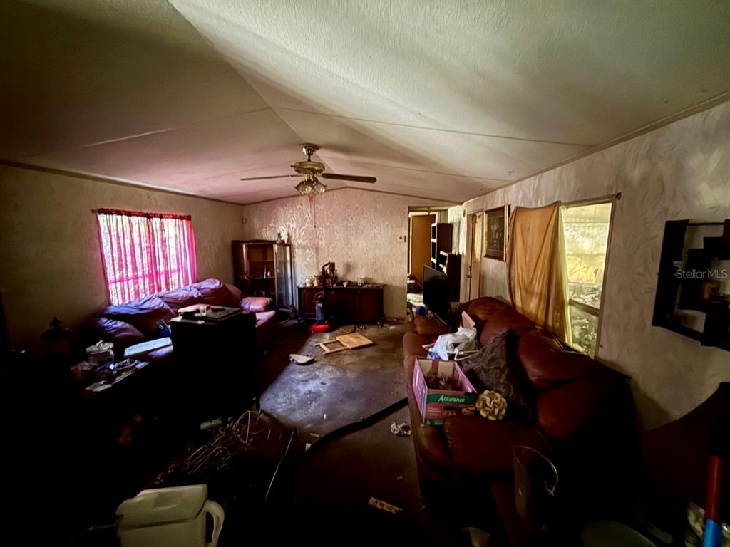 A living room with dark leather sofas, a ceiling fan, and worn flooring — 14051 NE 45TH PLACE, WILLISTON, FL