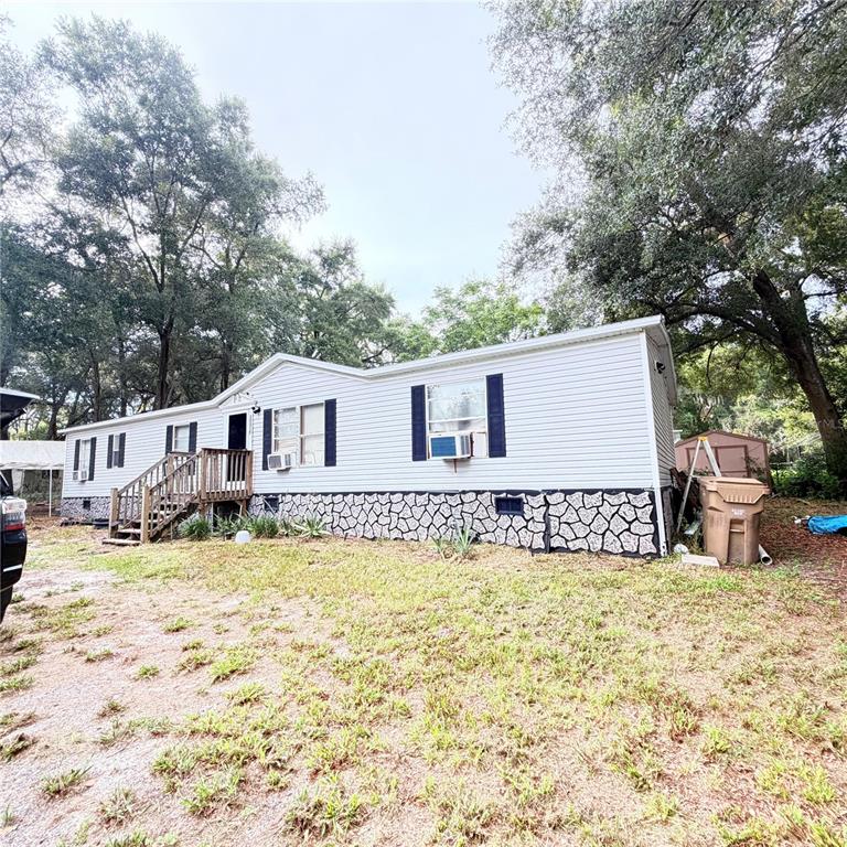 A single-story manufactured home with white siding and a stone-patterned foundation sits on a lot — 20315 GREENWING ROAD, ALTOONA, FL