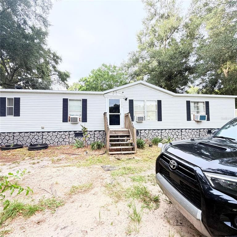 A white manufactured home with dark shutters and a stone-patterned skirting sits on a dirt lot — 20315 GREENWING ROAD, ALTOONA, FL
