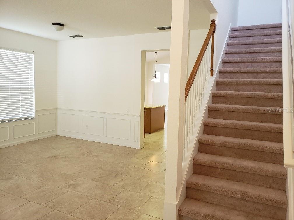 A carpeted staircase leads upstairs next to a room with tile flooring and wainscoting — 8625 GREENBANK BLVD, WINDERMERE, FL