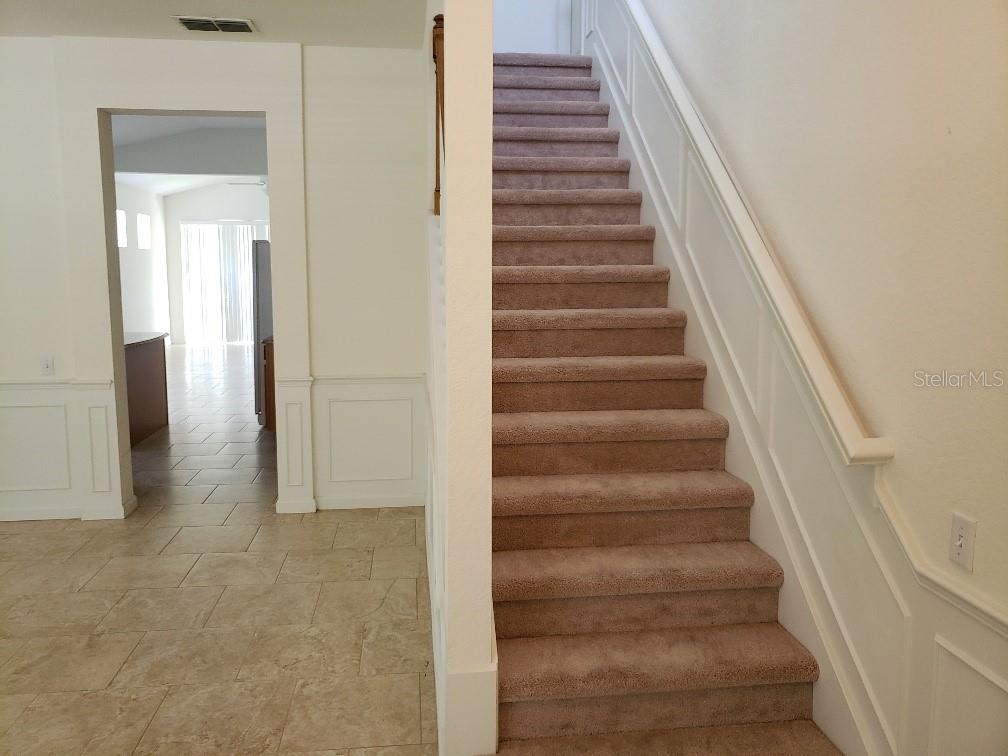 A carpeted staircase with white wainscoting sits beside a tiled entryway leading to another room — 8625 GREENBANK BLVD, WINDERMERE, FL
