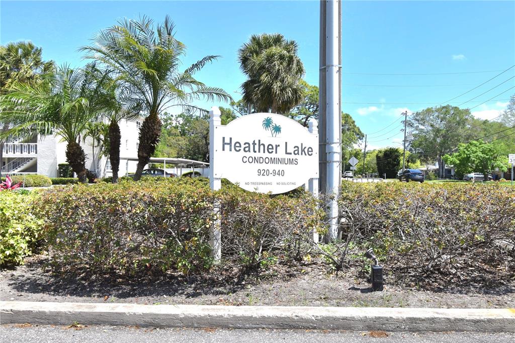 A sign for Heather Lake Condominiums stands in front of palm trees and landscaping — 940 VIRGINIA STREET UNIT 304, DUNEDIN, FL