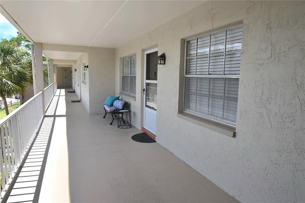 An exterior walkway with a white railing leads to a building entrance with windows — 940 VIRGINIA STREET UNIT 304, DUNEDIN, FL