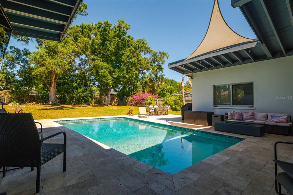 A backyard features a rectangular swimming pool, stone patio, outdoor seating, and a shade sail — 1424 S EVERGREEN AVENUE, CLEARWATER, FL