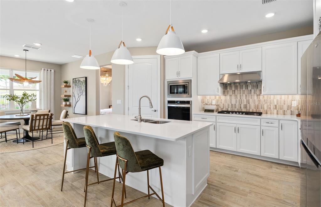 A modern kitchen features white cabinetry, a large island with bar stools, and tile flooring — 5095 TWIN LAKES BOULEVARD, ST CLOUD, FL