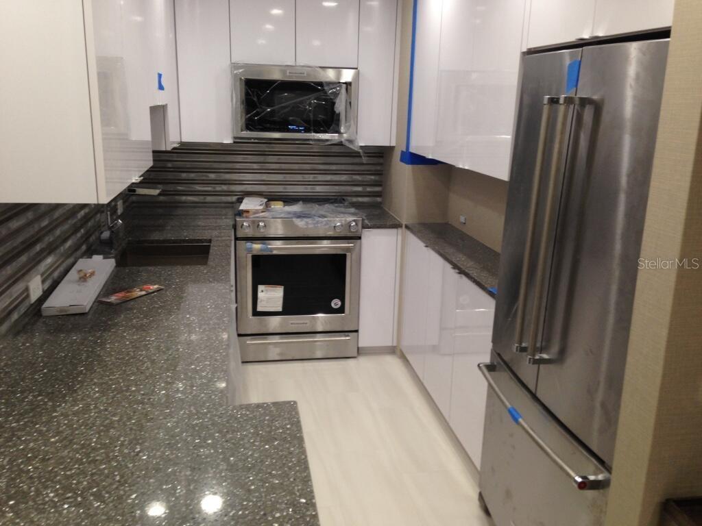 A modern kitchen features white cabinets, stainless steel appliances, and dark speckled countertops — 4015 BAYSHORE UNIT 17A, TAMPA, FL
