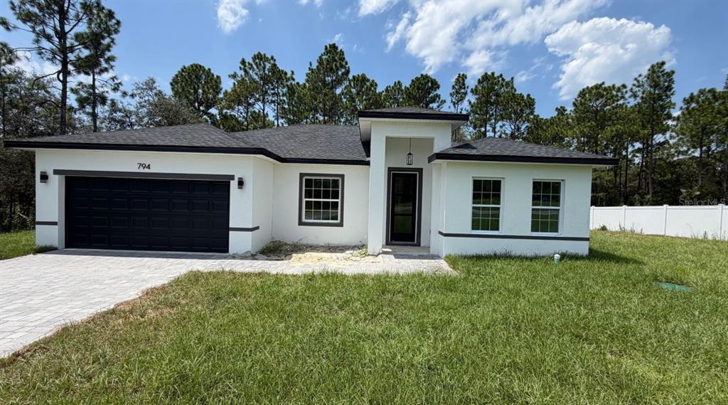 A single-story house with white stucco walls, a black garage door, and a dark roof — 794 MARION OAKS MANOR, OCALA, FL