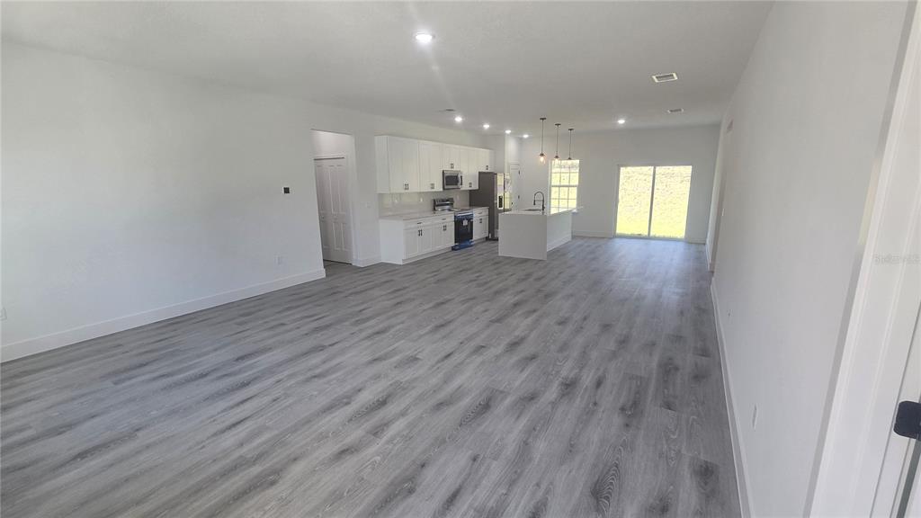 An open-concept kitchen and living area features white cabinets, a central island, and gray flooring — 794 MARION OAKS MANOR, OCALA, FL